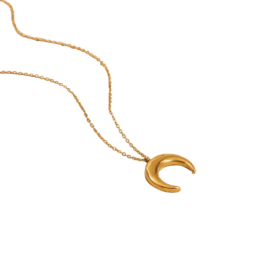 Gold necklace with a crescent moon pendant on a textured beige surface