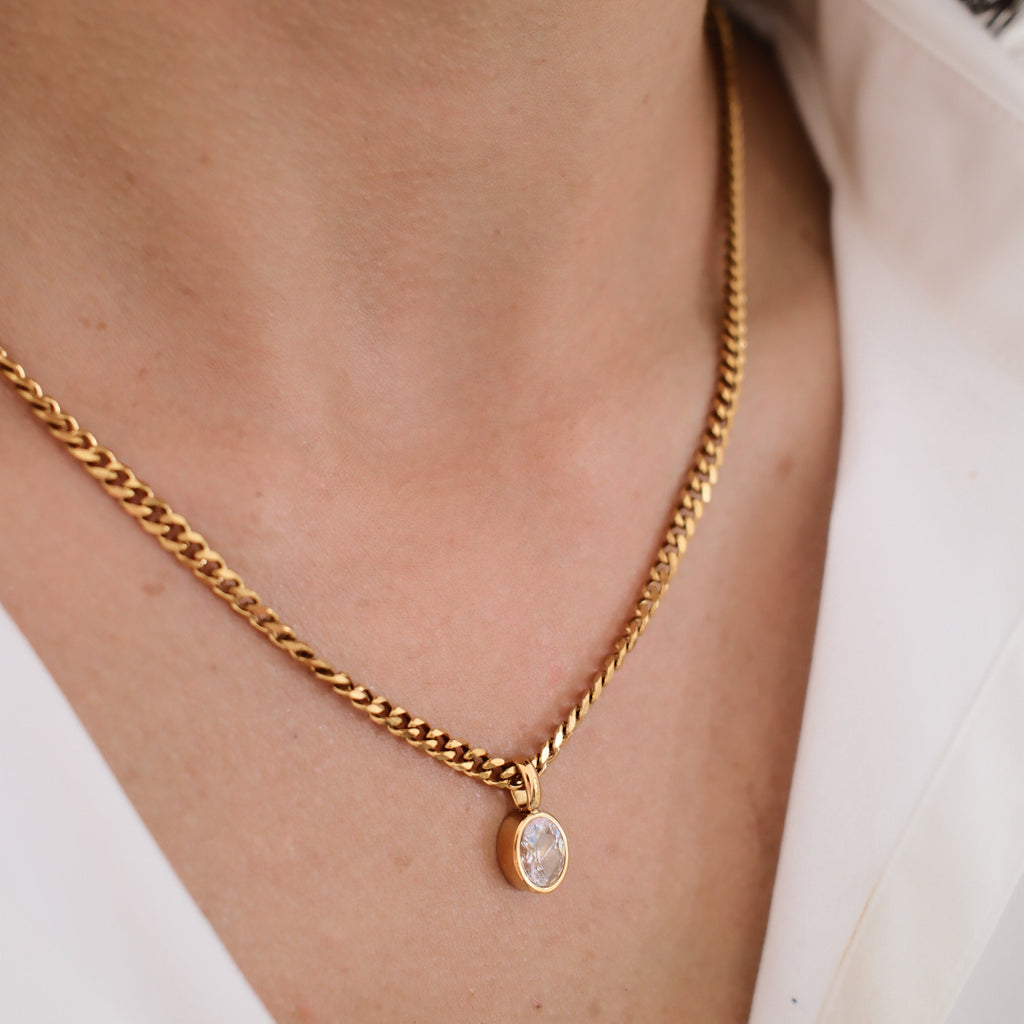 Gold chain necklace with a pendant worn by a person in a white shirt.