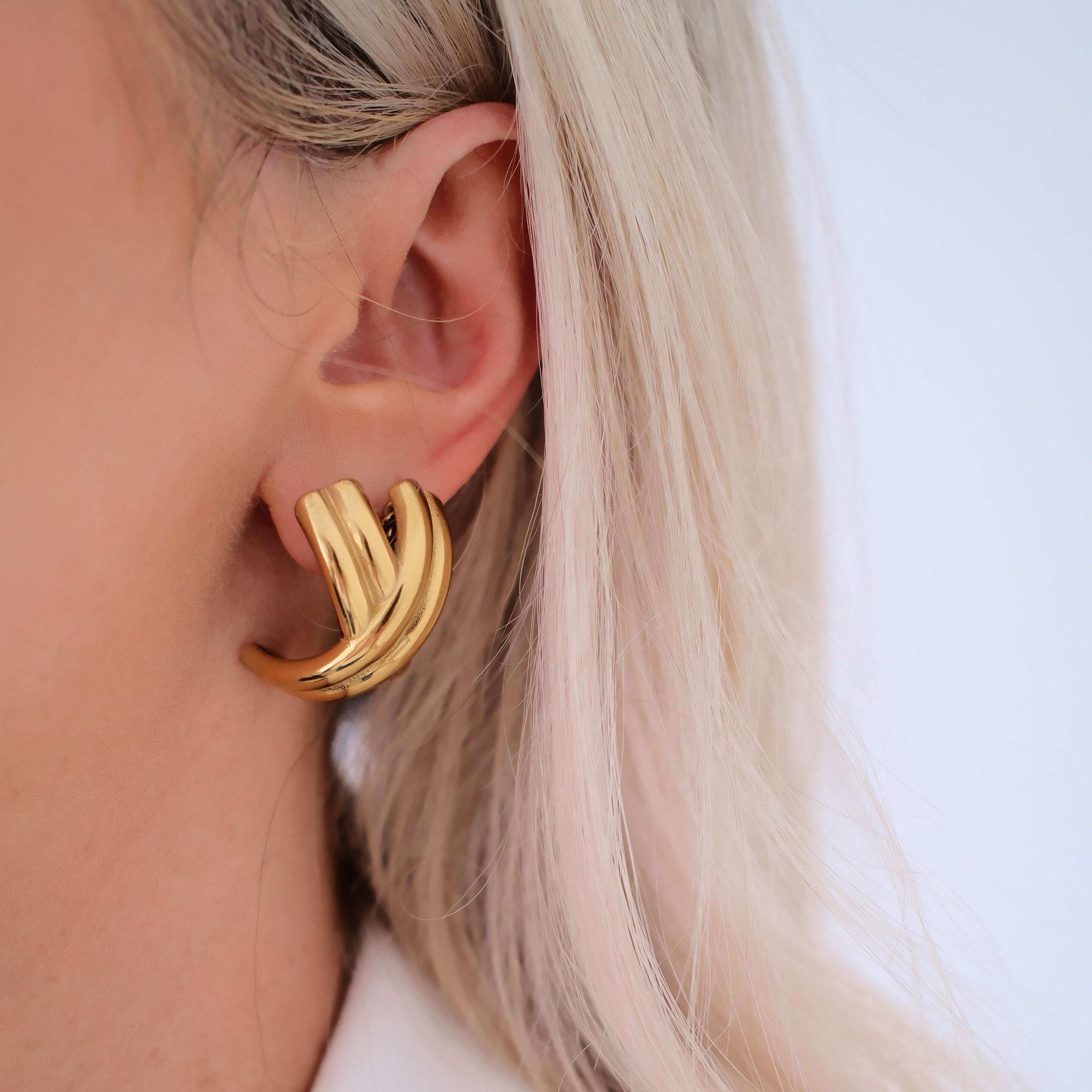Gold hoop earring worn by a person with blonde hair on a white background