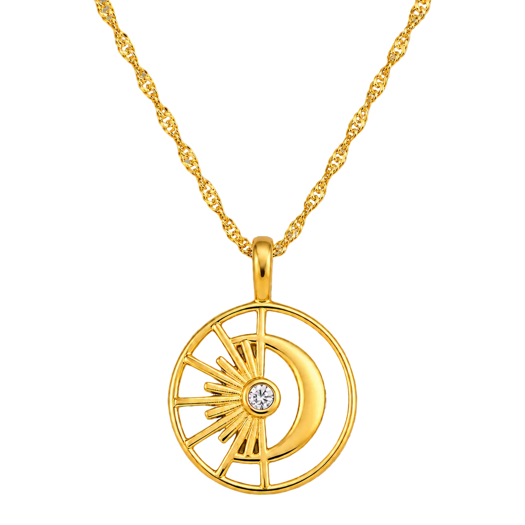 A gold pendant necklace featuring a circular design with a crescent moon, sunburst rays, and a small clear gemstone at the center, displayed on a textured gray background.